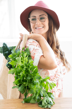 Natalie K. Douglas smiling while carrying a bag of green vegetables and wearing a Boho outfit with glasses